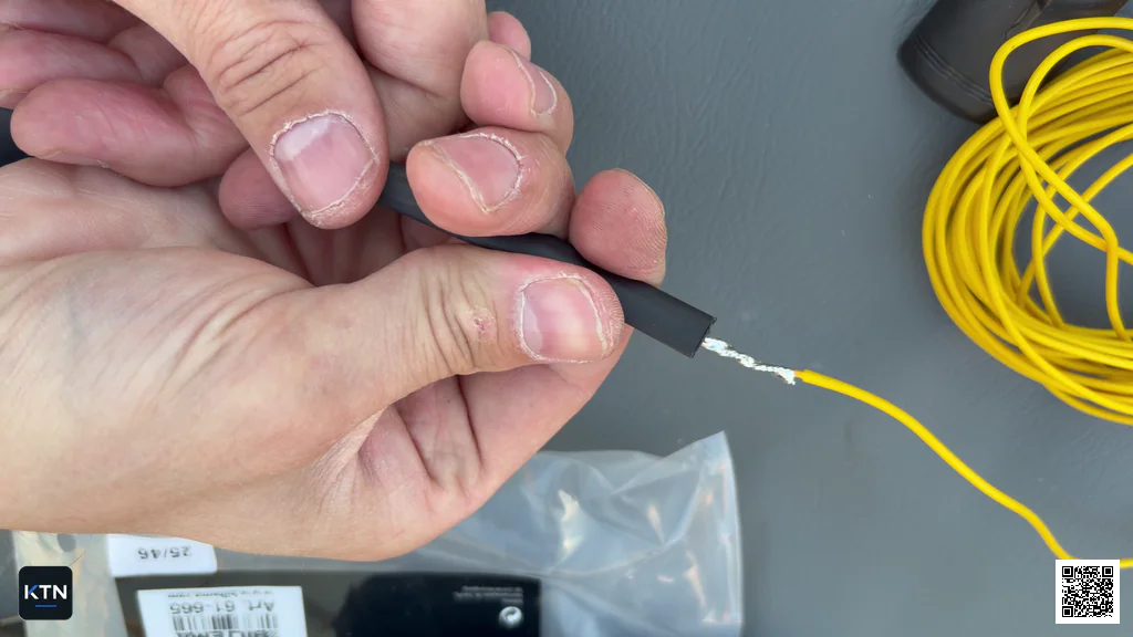 Black heat-shrink tubing being slid over the cooled wire splice